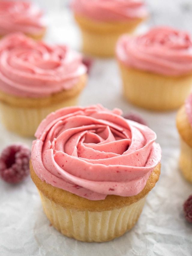 Raspberry lemon cupcakes with pink raspberry frosting next to some raspberries.