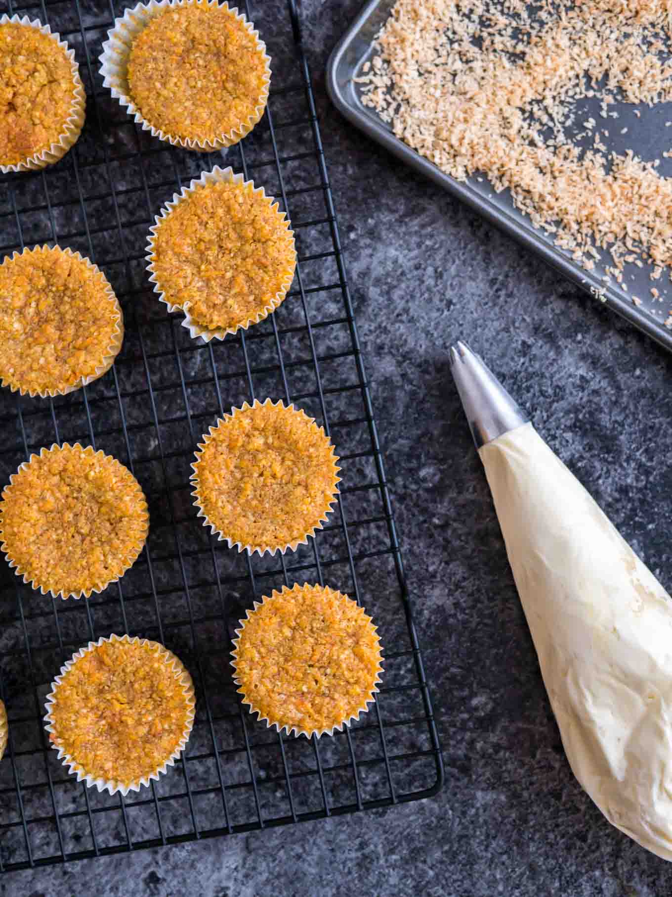 Cupcakes on a cooling rack next to a pastry piping bag.