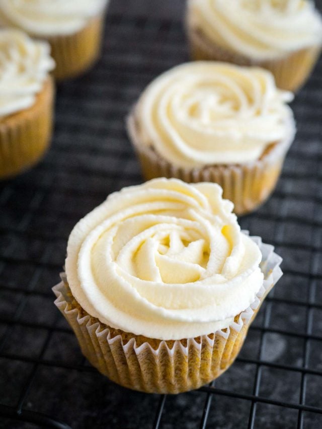 Carrot cake cupcakes, topped with cream cheese frosting sitting on a black cooling rack