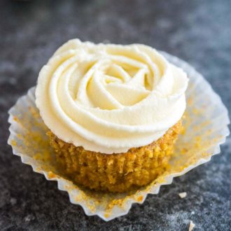 Un cupcake de pastel de zanahoria con glaseado de queso crema en la parte superior. El papel está doblado lejos de la magdalena y está sentado en una superficie gris oscuro.