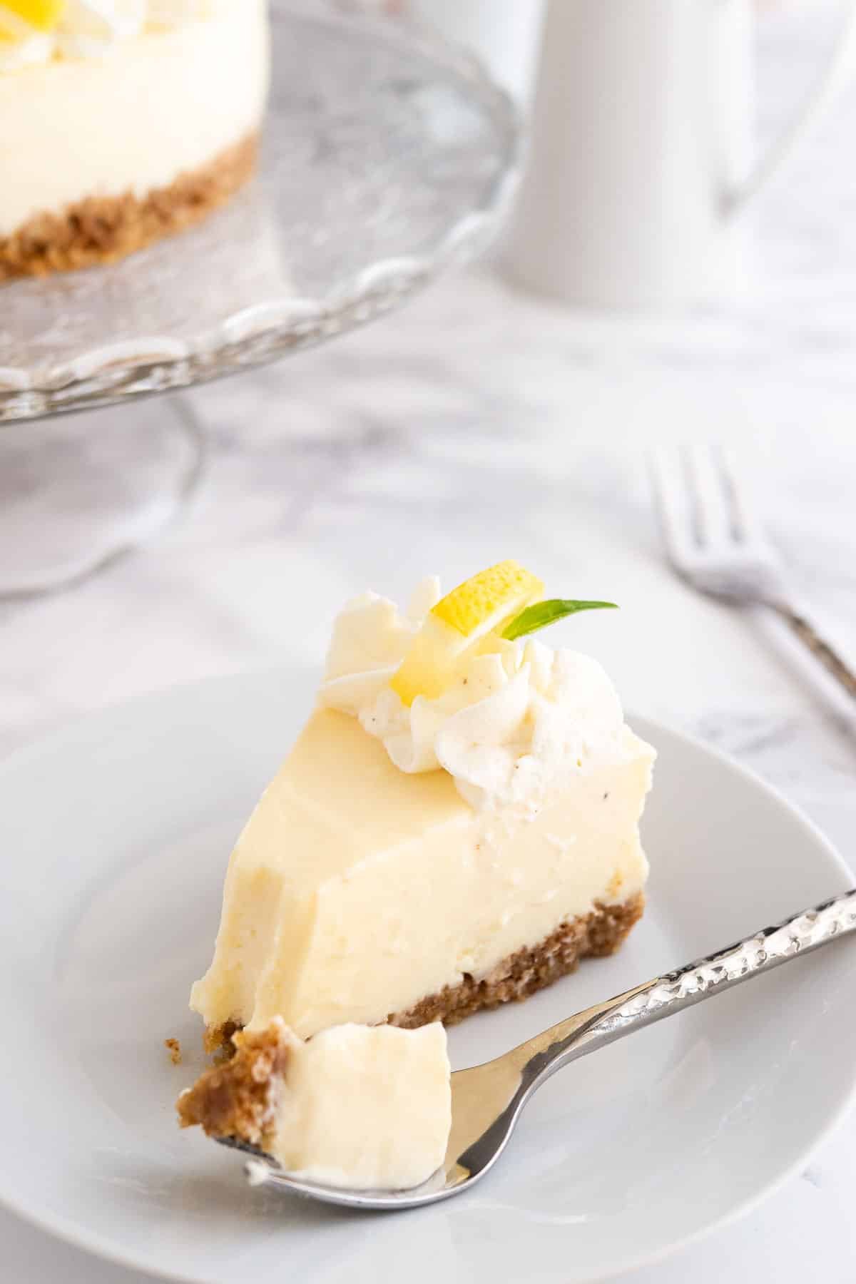 A slice of lemon cream pie on a white plate with a fork on a marble surface. 