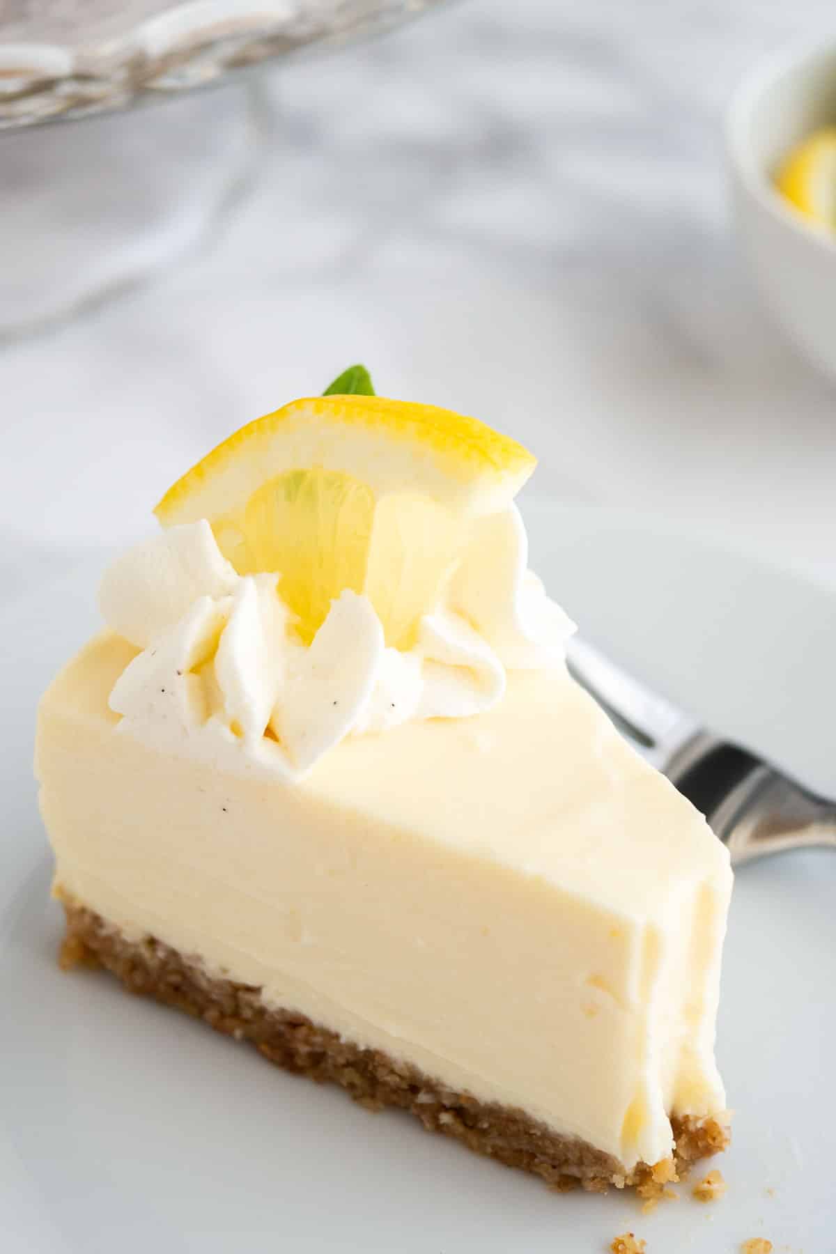 Close-up of A slice of lemon cream pie on a white plate with a fork on a marble surface.