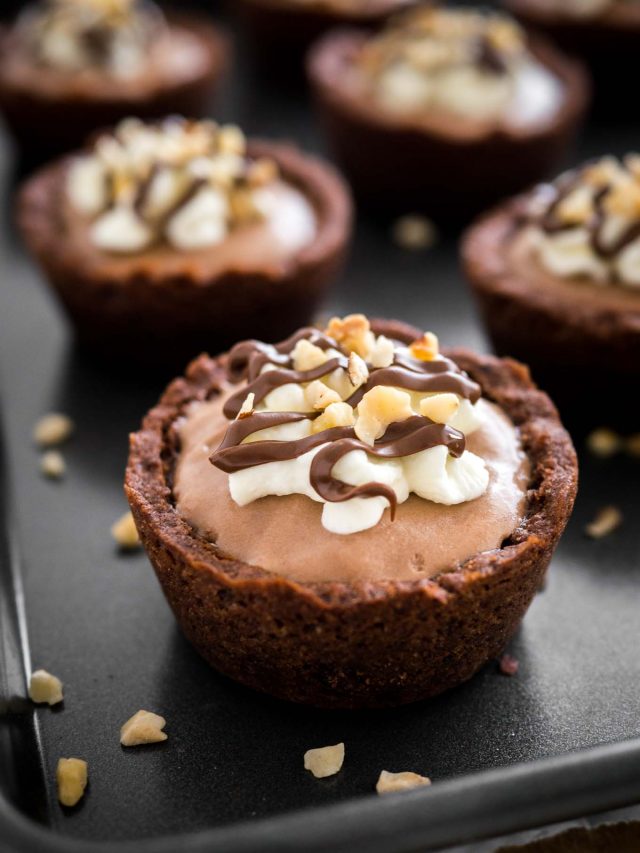 Close-up of a nutella mousse cookie cup on a black surface. There are more cookie cups in the background.