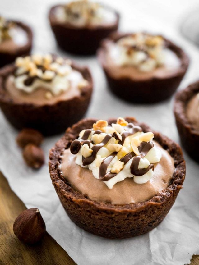 Close-up of a nutella mousse cookie cup on parchment paper. There are more cookie cups and a jar of nutela in the background.