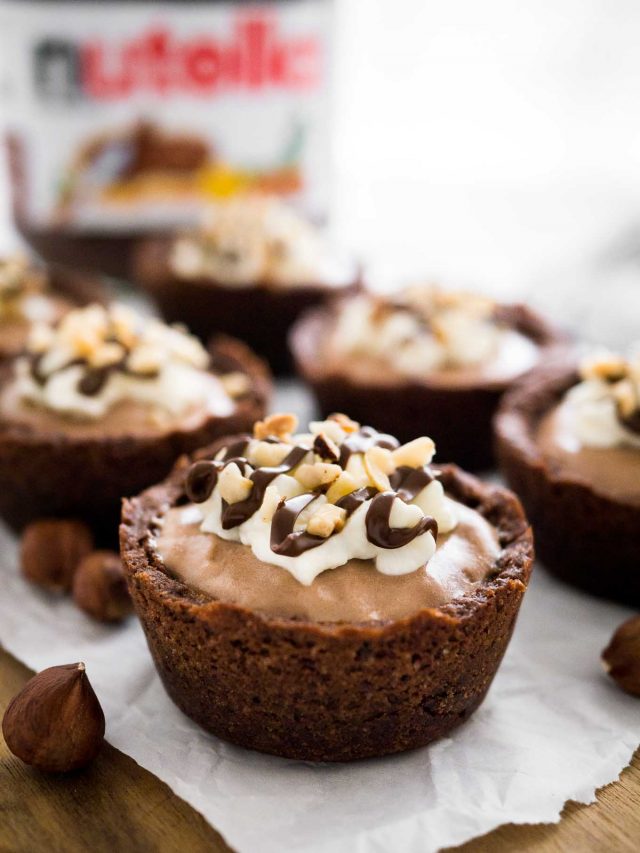 Close-up of a nutella mousse cookie cup on parchment paper. There are more cookie cups and a jar of nutela in the background.