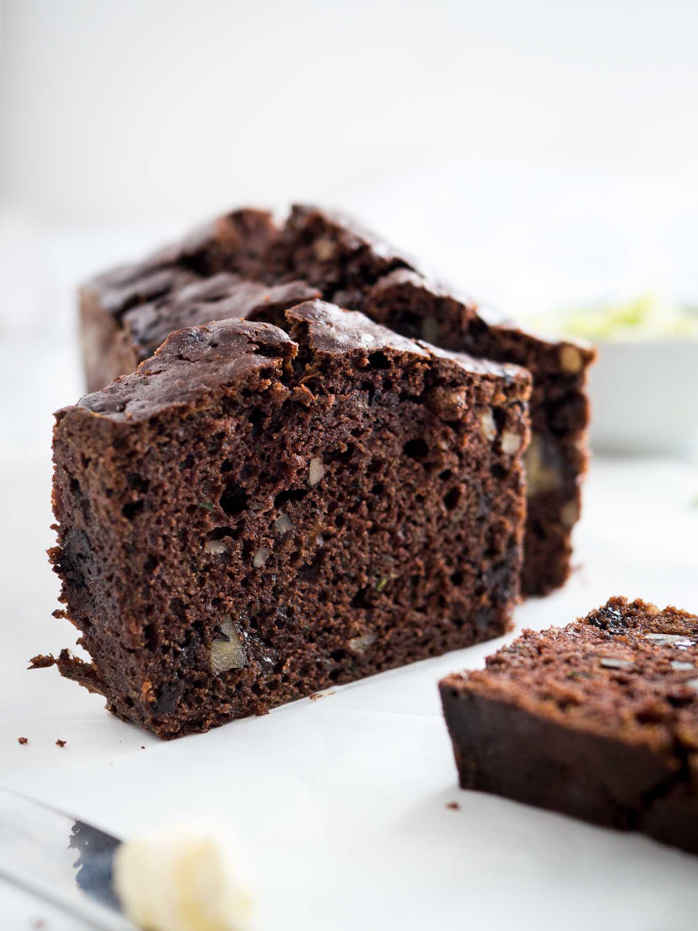 A loaf of chocolate zucchini bread with two slices cut off, one standing one lying in front.