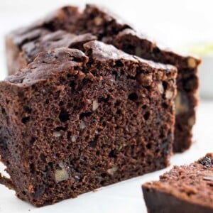 Close-up of a loaf of chocolate zucchini bread with two slices cut off, one standing one lying in front.