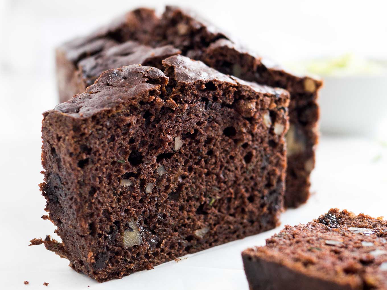 Close-up of a loaf of chocolate zucchini bread with two slices cut off, one standing one lying in front.