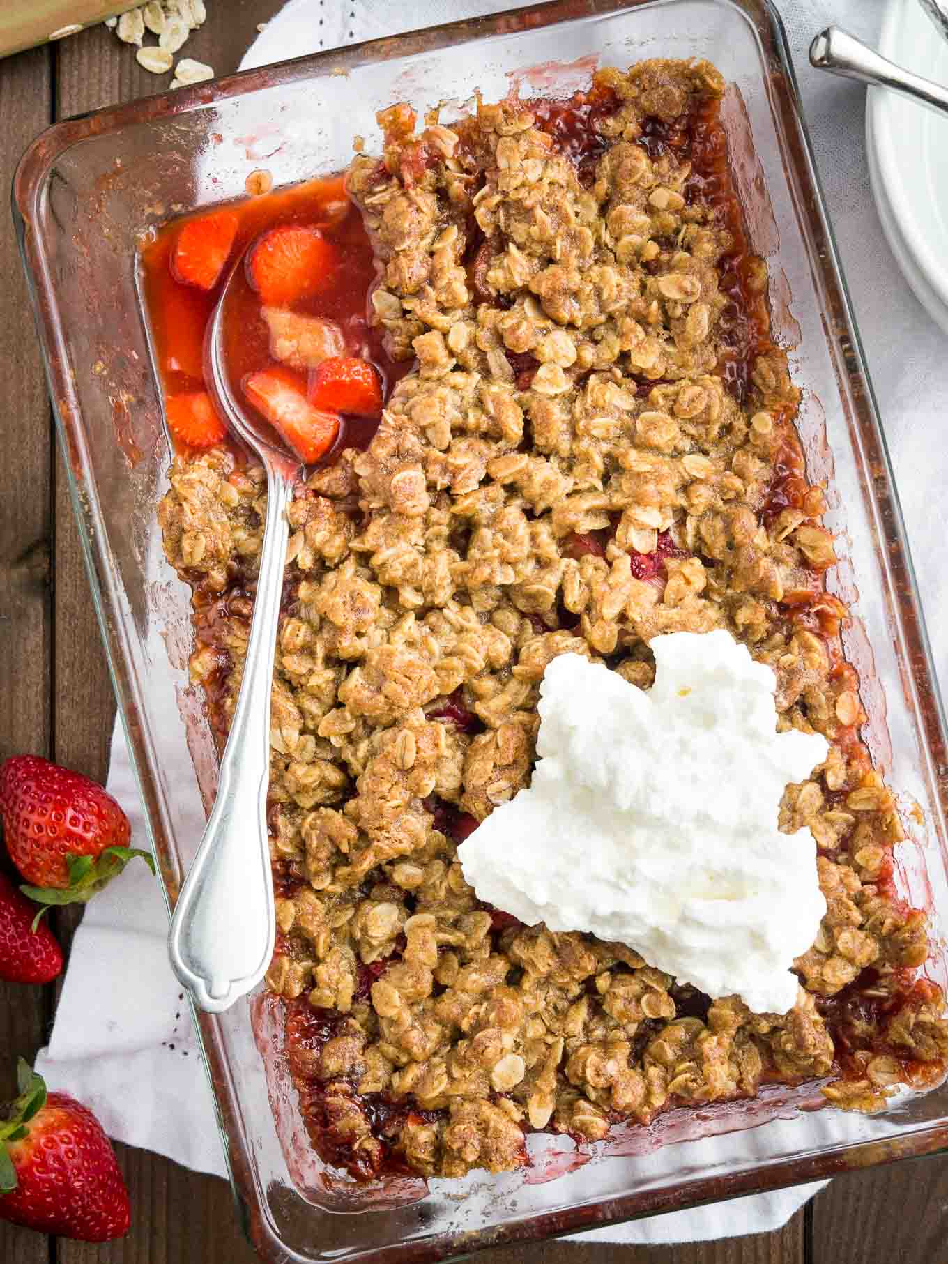 Strawberry rhubarb crisp in a glass baking dish on a wooden table. 