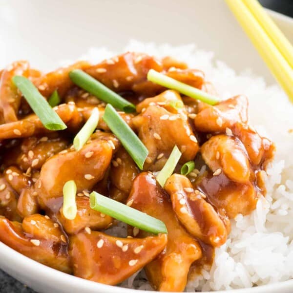 A grey bowl with rice and general tso's chicken, garnished with chives, with chopsticks.