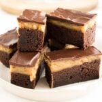 A grey plate of peanut butter brownie bars in front of a wooden cutting board.