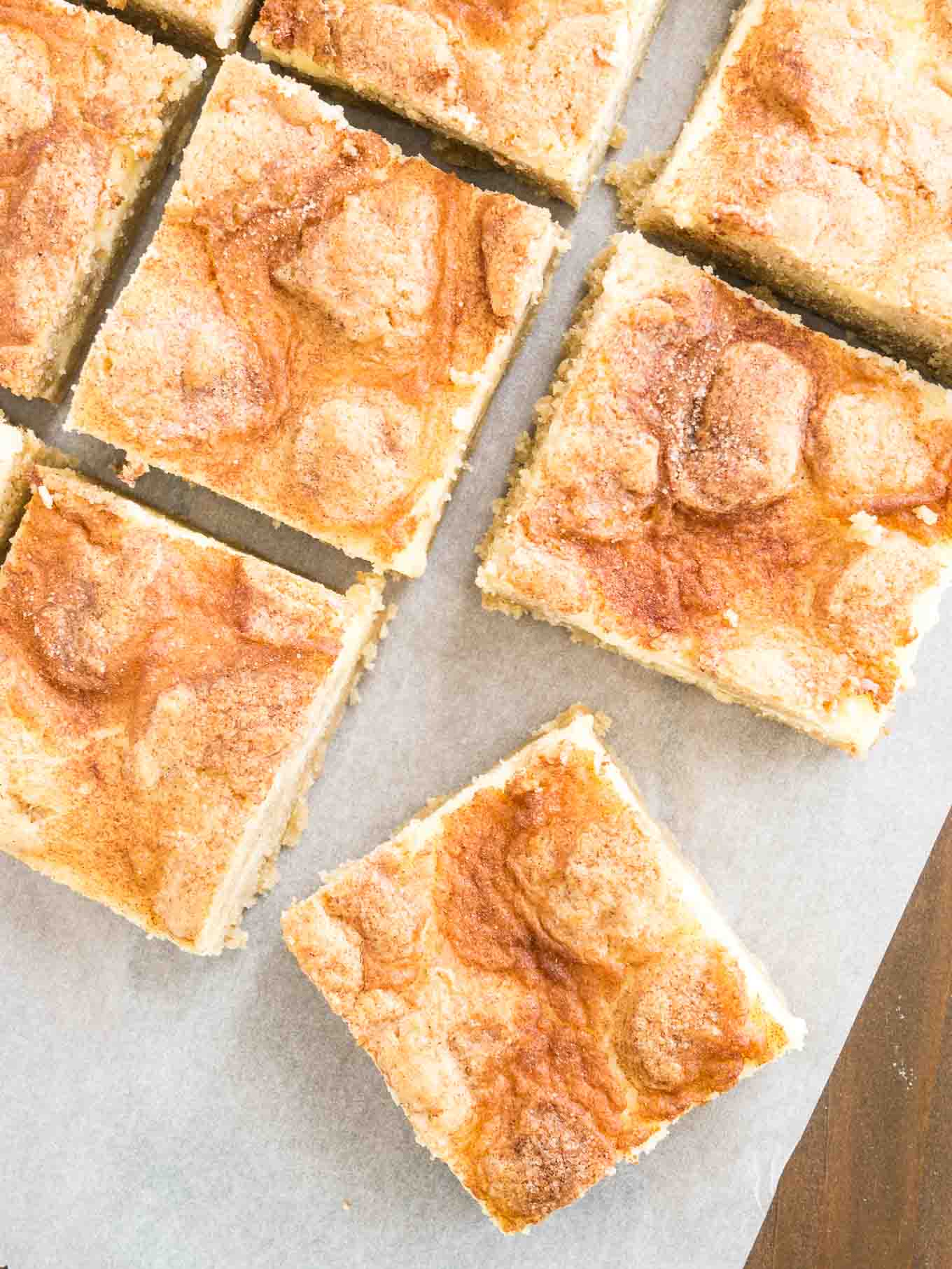 Top-down shot of some snickerdoodle cheesecake bars sitting on parchment paper. The frontmost is turned 45 degrees.