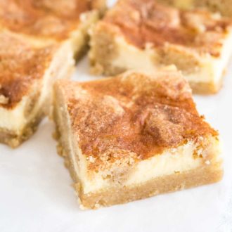 Some snickerdoodle cheesecake bars sitting on parchment paper. The frontmost is turned 45 degrees.