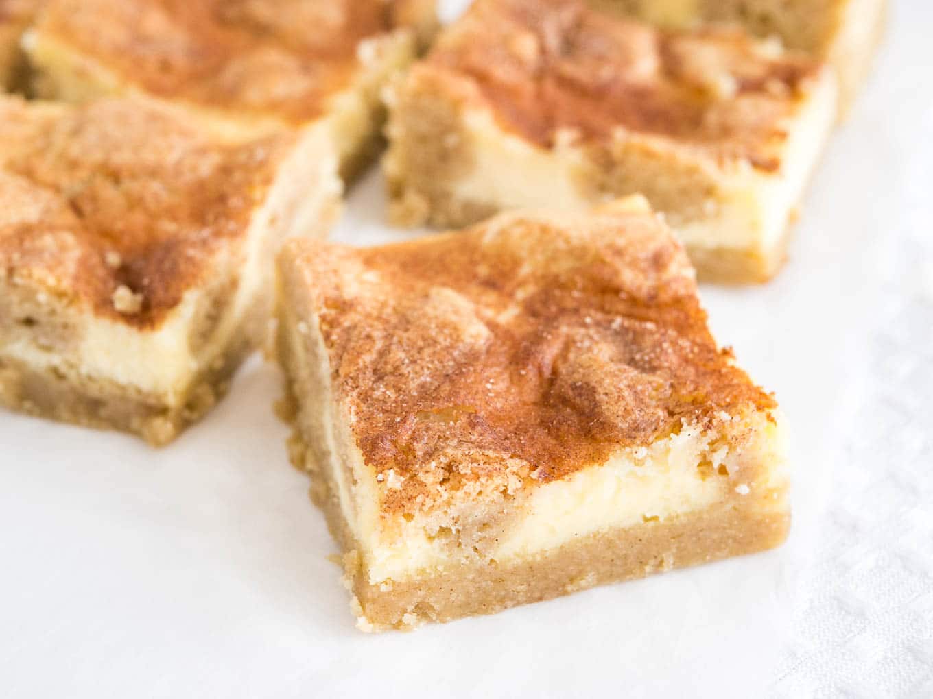 Some snickerdoodle cheesecake bars sitting on parchment paper. The frontmost is turned 45 degrees.