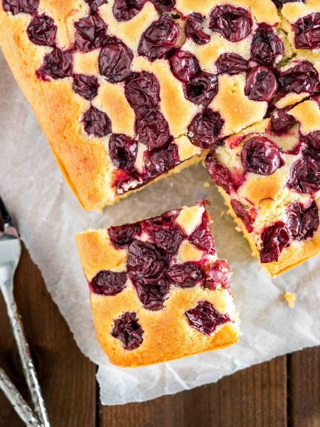 Top-down shot of cherry cake with a square cut out and placed at an angle on some parchment with a fork.