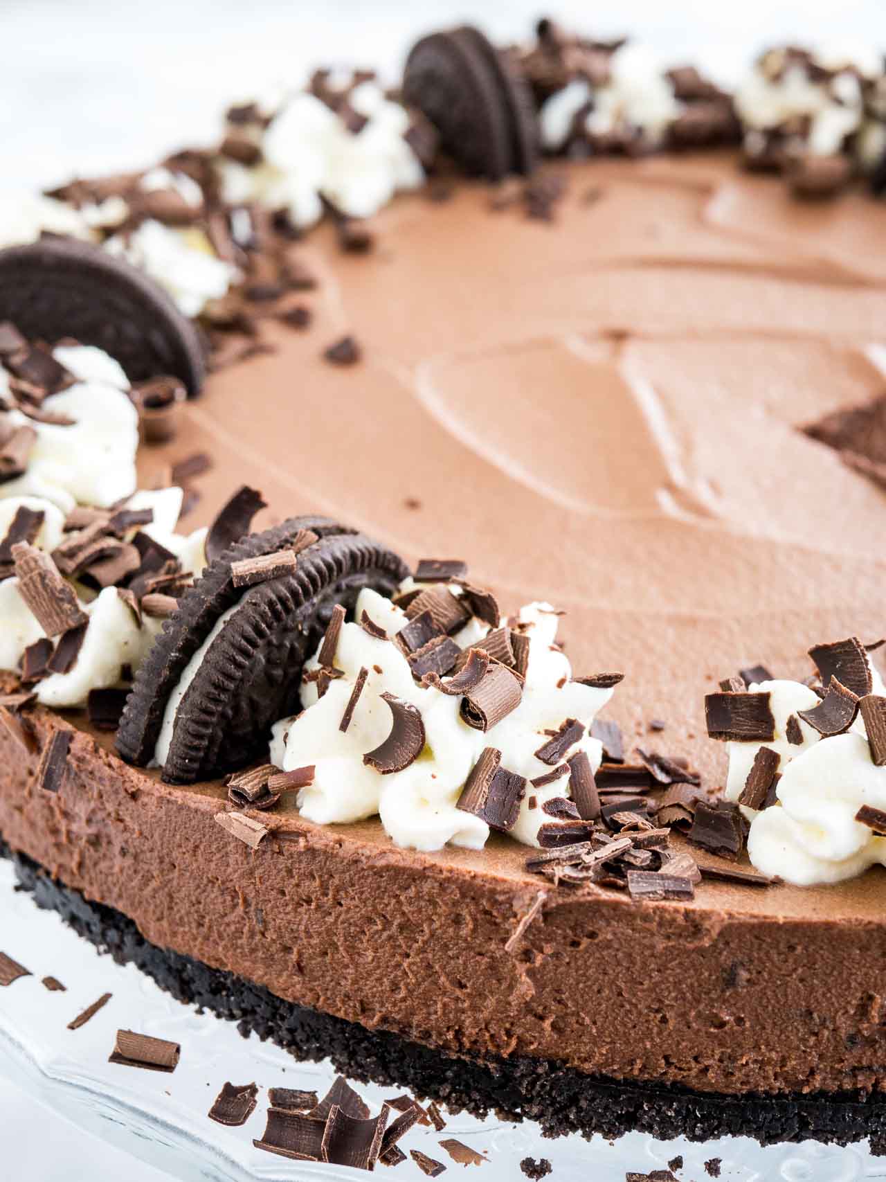 Close-up of chocolate mousse cake with Oreo crust, topped with halved Oreo cookies, whipped cream and chocolate shavings.