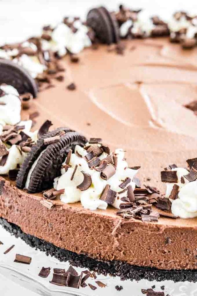 Close-up of chocolate mousse cake with oreo crust, topped with halved oreo cookies, whipped cream and chocolate shavings.