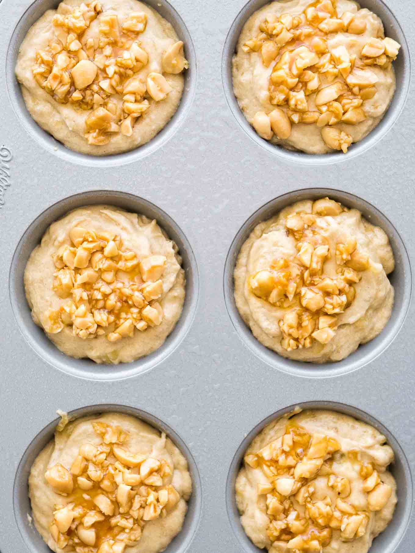 Top-down shot of a grey muffin pan with muffin batter topped with peanuts before baking.