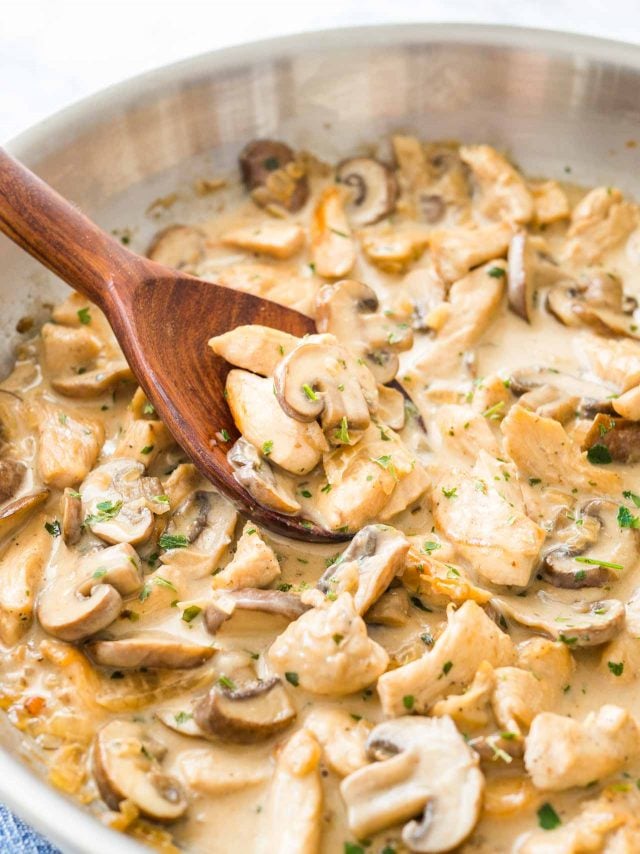 Mushroom Chicken Pasta sauce with cream in a stainless steel pan, with a wooden cooking spoon in it.