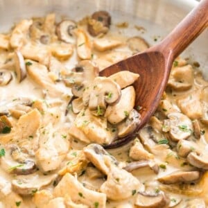 Mushroom Chicken Pasta sauce with cream in a stainless steel pan, with a wooden cooking spoon in it.