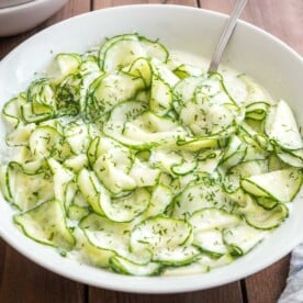 German Cucumber salad in a white salad bowl on a wooden table with a spoon in it