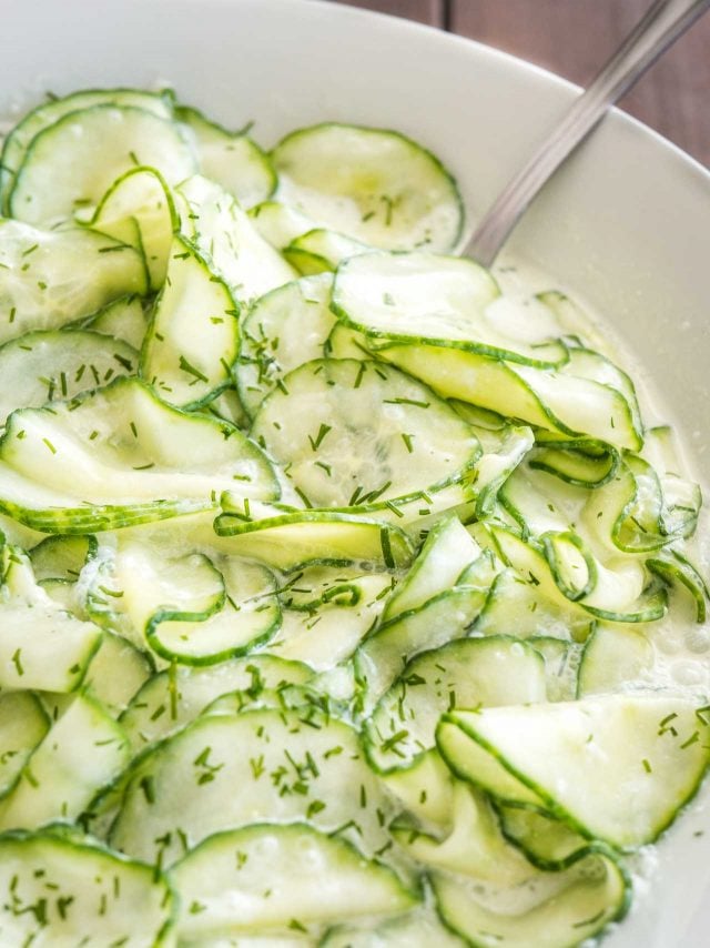 Close-up of German cucumber salad in a white salad bowl with a spoon in it