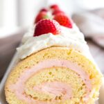 Close-up of a strawberry swiss cake roll topped with whipped cream and strawberries on a rectangular serving platter.