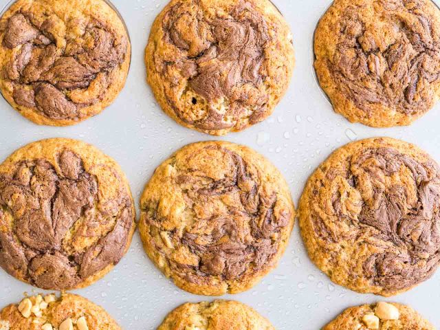 Top-down shot of a grey muffin pan with banana nutella muffins in it after baking.