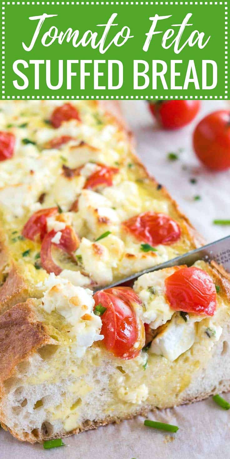 Image with text: Tomato feta stuffed bread, image: A bread knife cutting into tomato feta stuffed french bread garnished with tomatoes and chives on a bamboo cutting board lined with parchment paper.