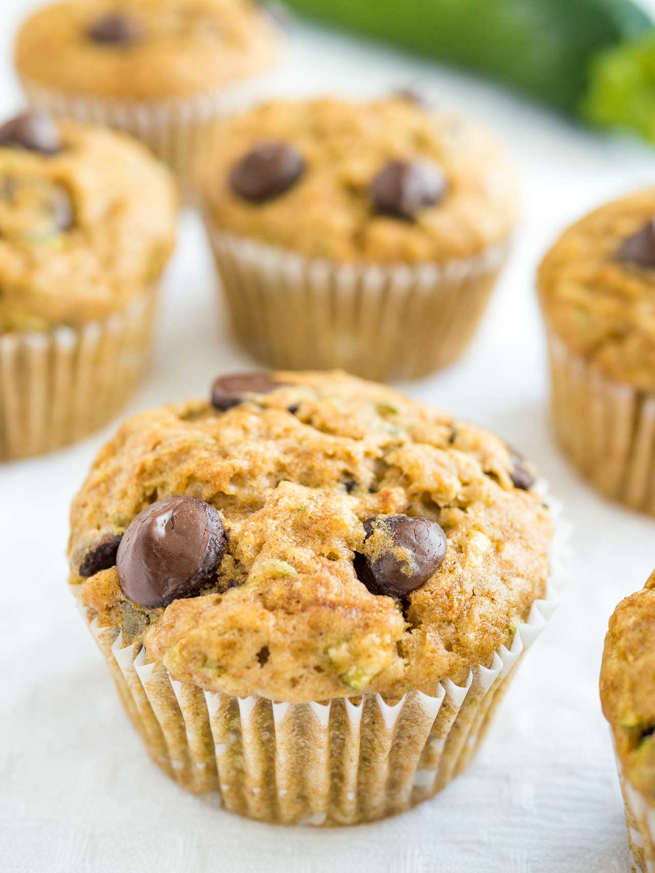 Close-up of zucchini chocolate chip muffins on a white tablecloth with zucchini in the background.