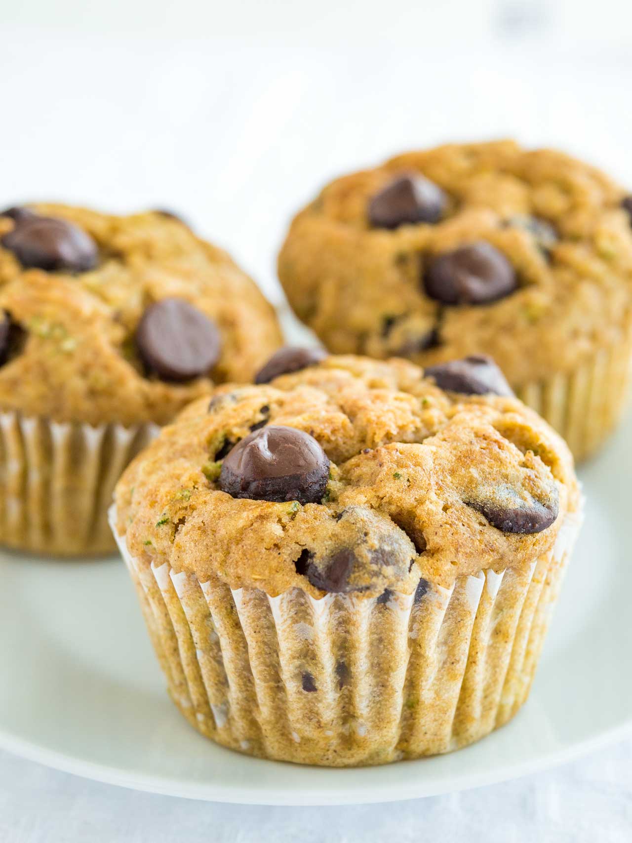 Close up of zucchini chocolate chip muffins on a white plate.