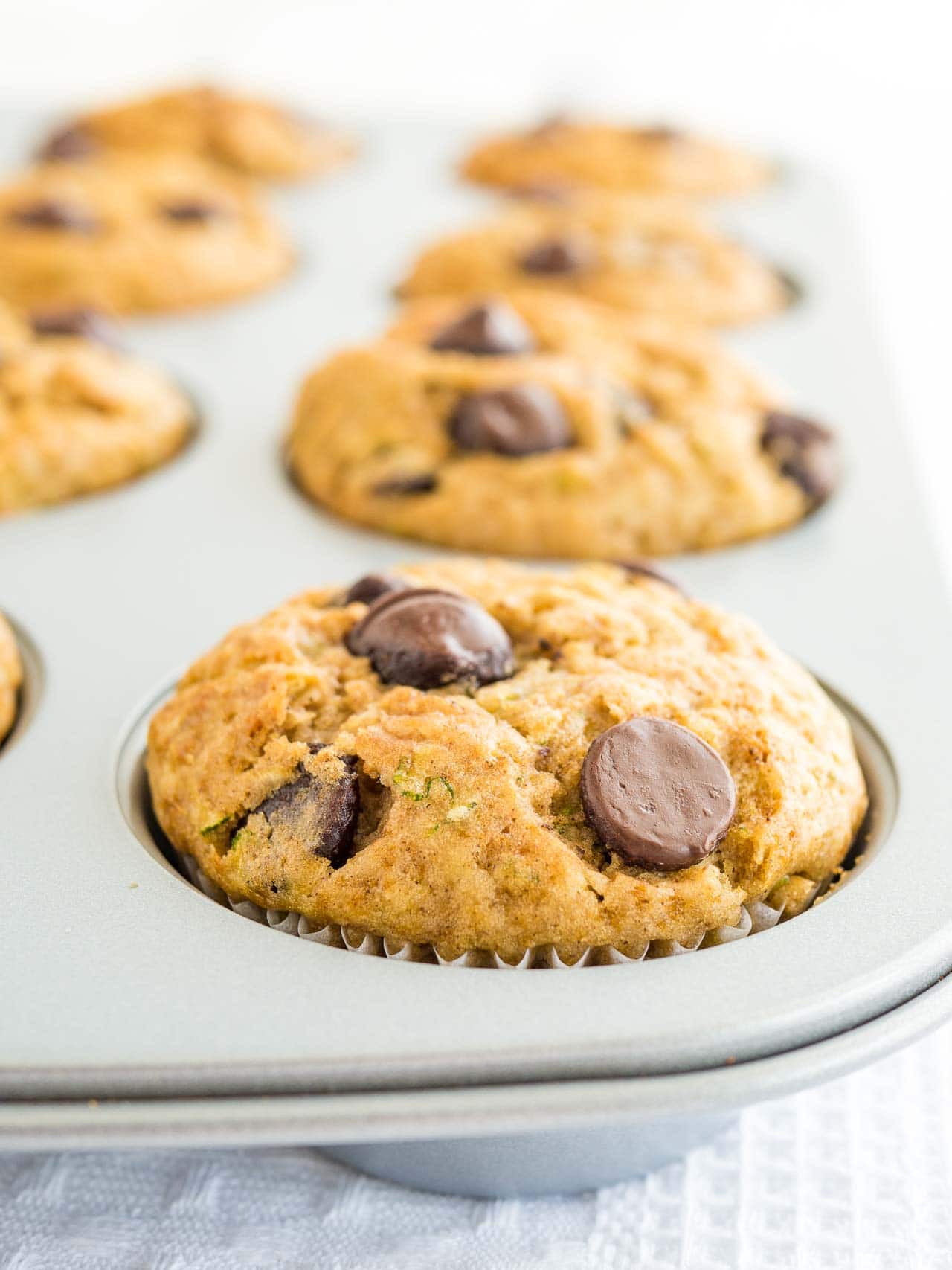 A grey muffin pan with zucchini chocolate chip muffins.