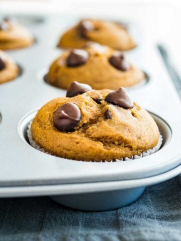 A grey muffin pan with pumpkin chocolate chip muffins on a grey dishtowel.