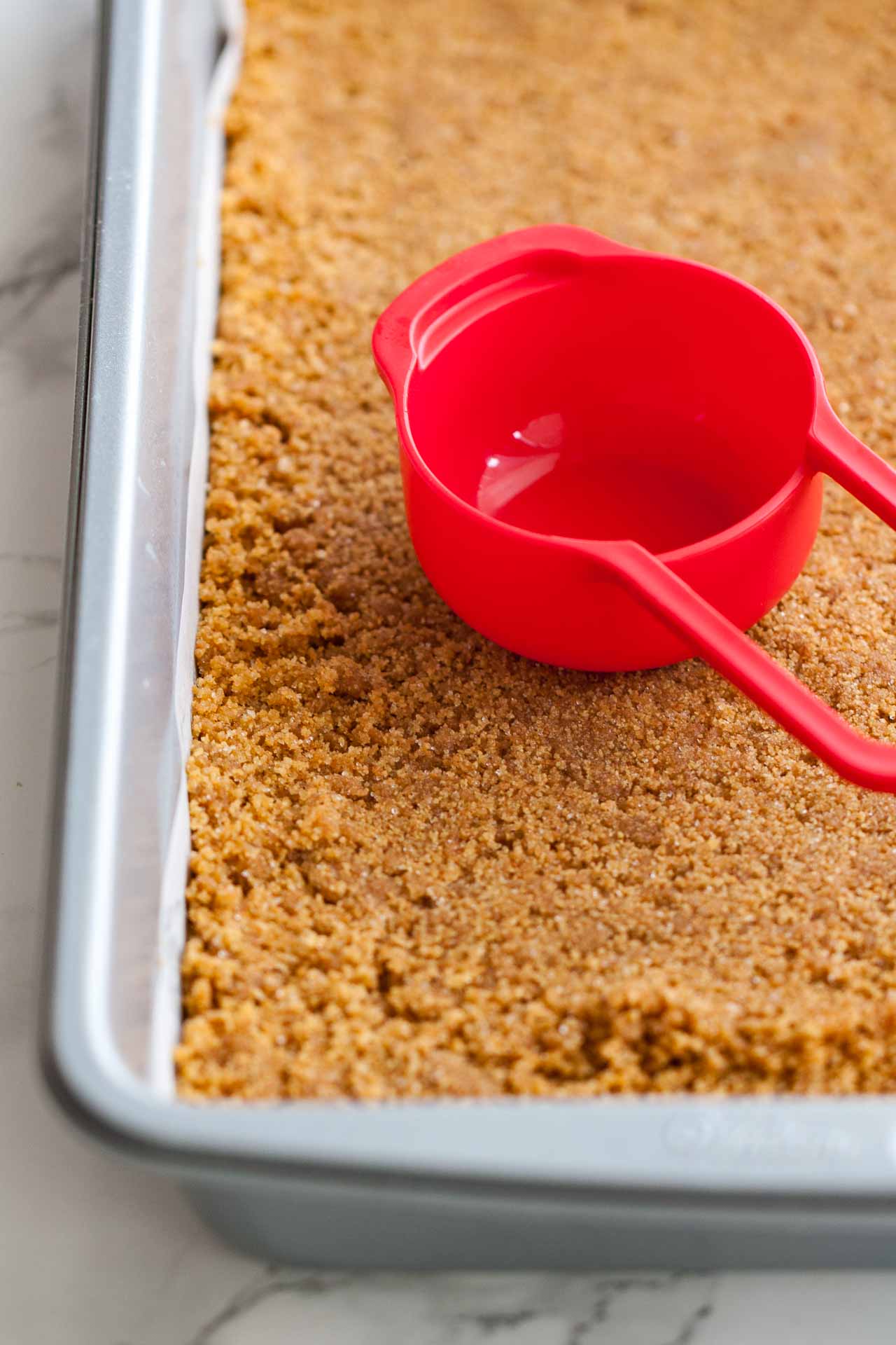 A baking sheet with a graham cracker crust and a red measuring cup.