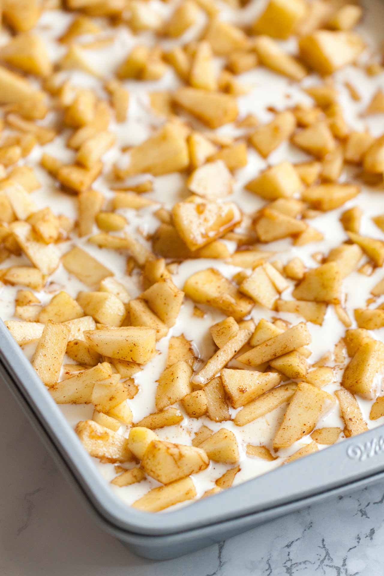 A baking sheet with a cheesecake layer topped with apple pieces.