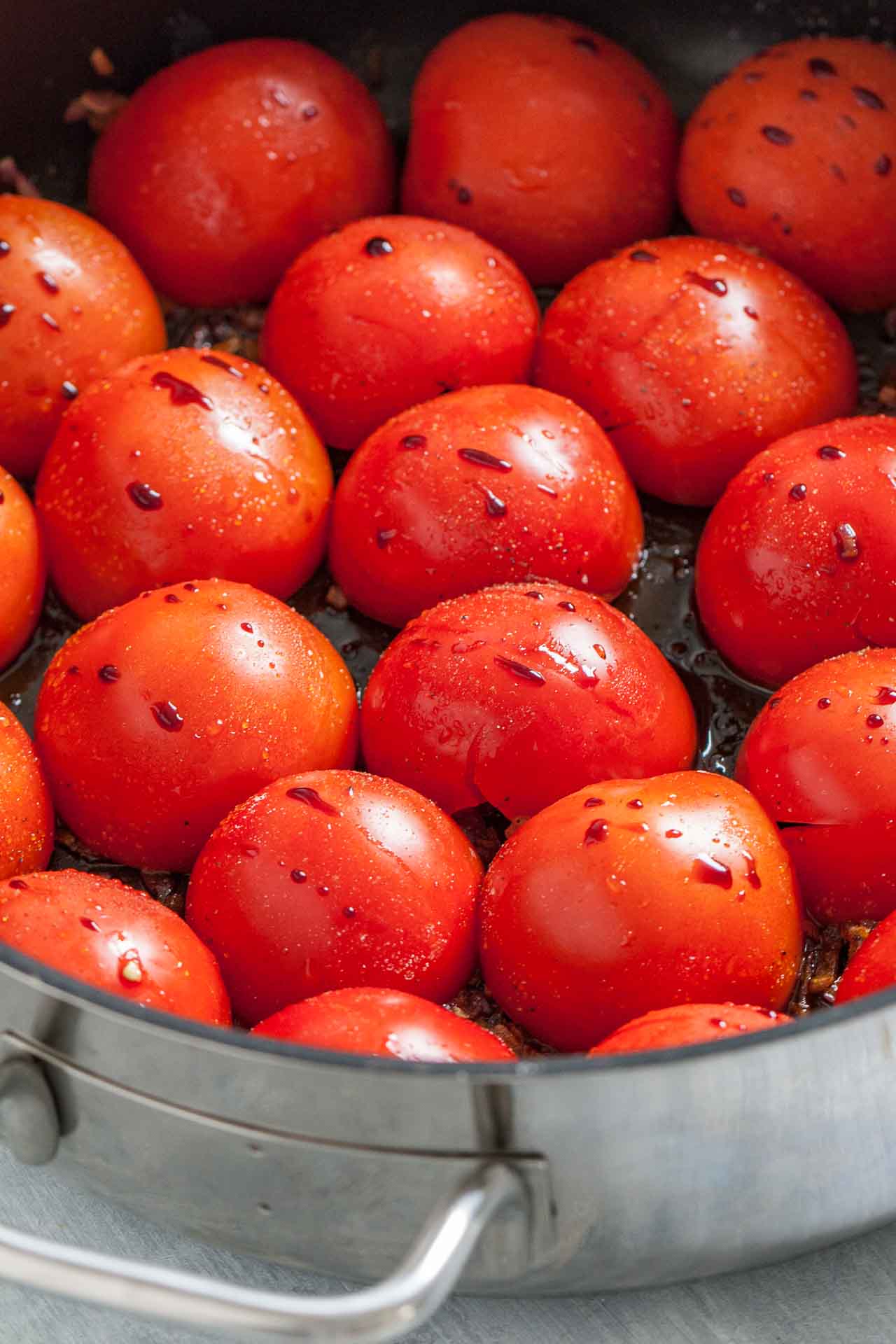 A pan of halved tomatoes lying cut side down, with some balsamic vinegar.