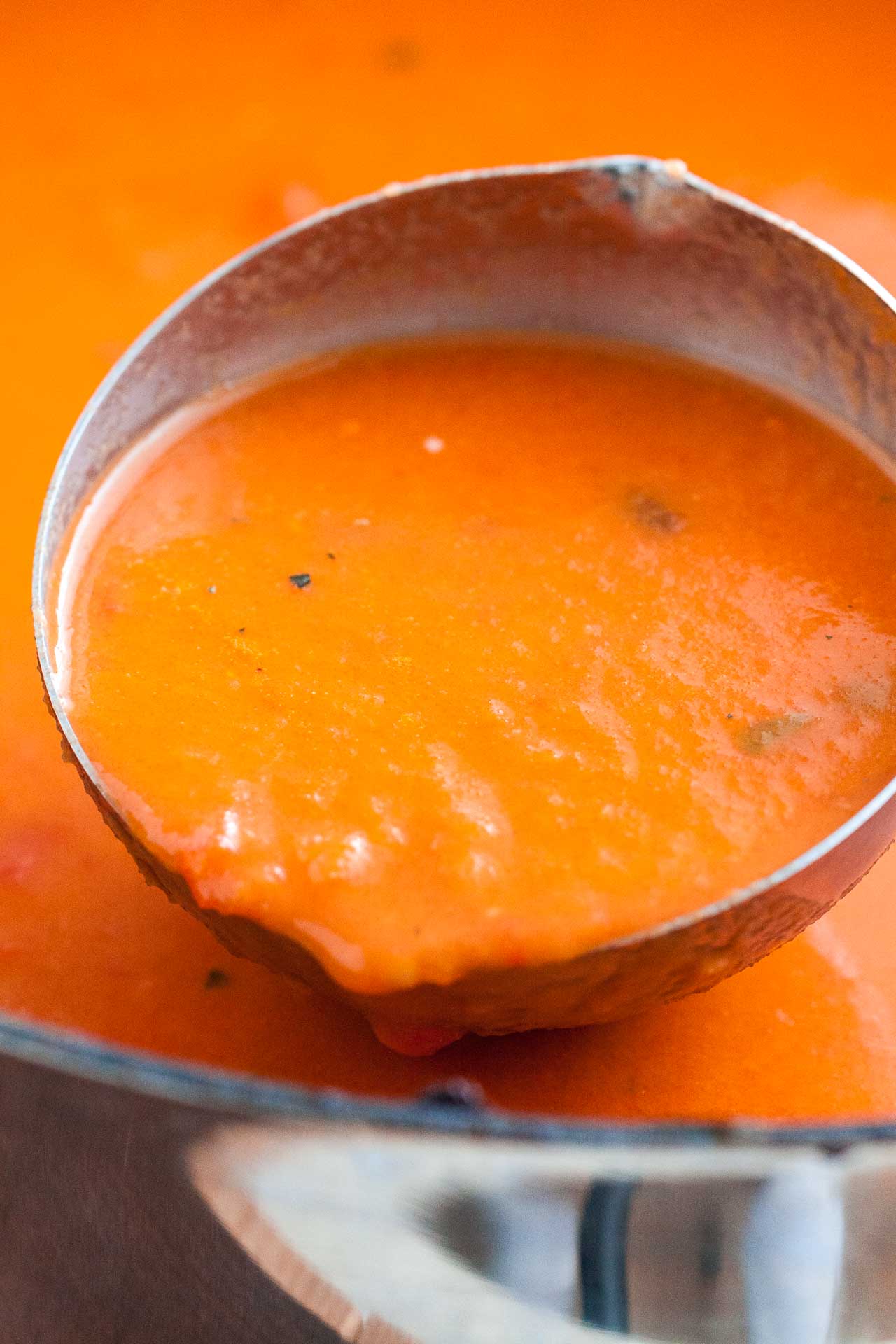 Close up of a ladle scooping tomato soup out of a pot.