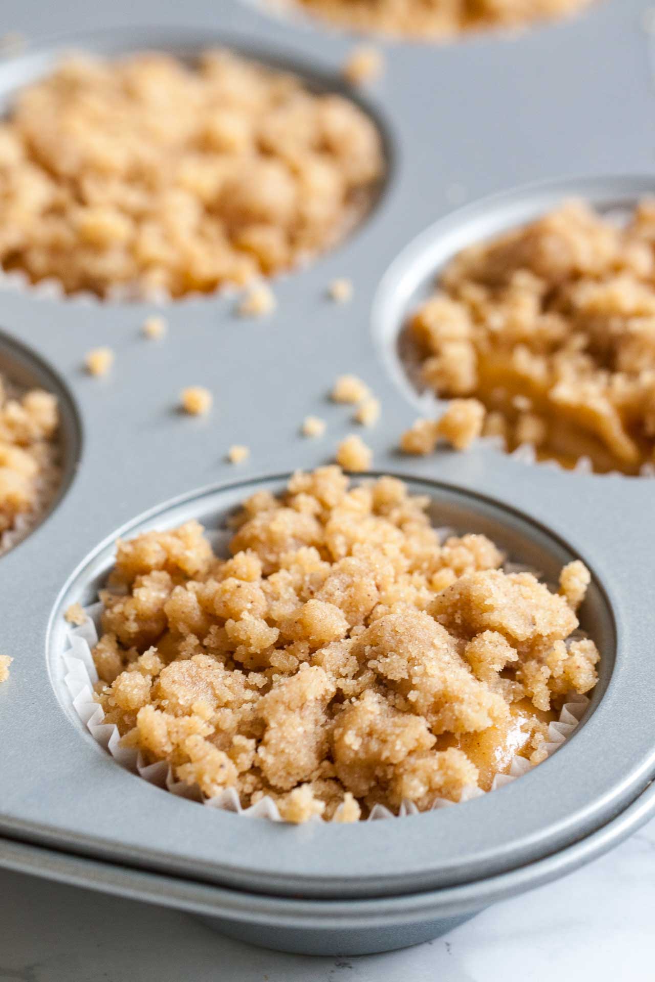 Close-up of a muffin pan with pumpkin spice muffins with streusel topping photographed before baking.