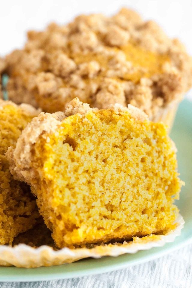 Close-up of a halved pumpkin spice muffin leaning against a pumpkin spice muffin topped with streusel on a teal plate.