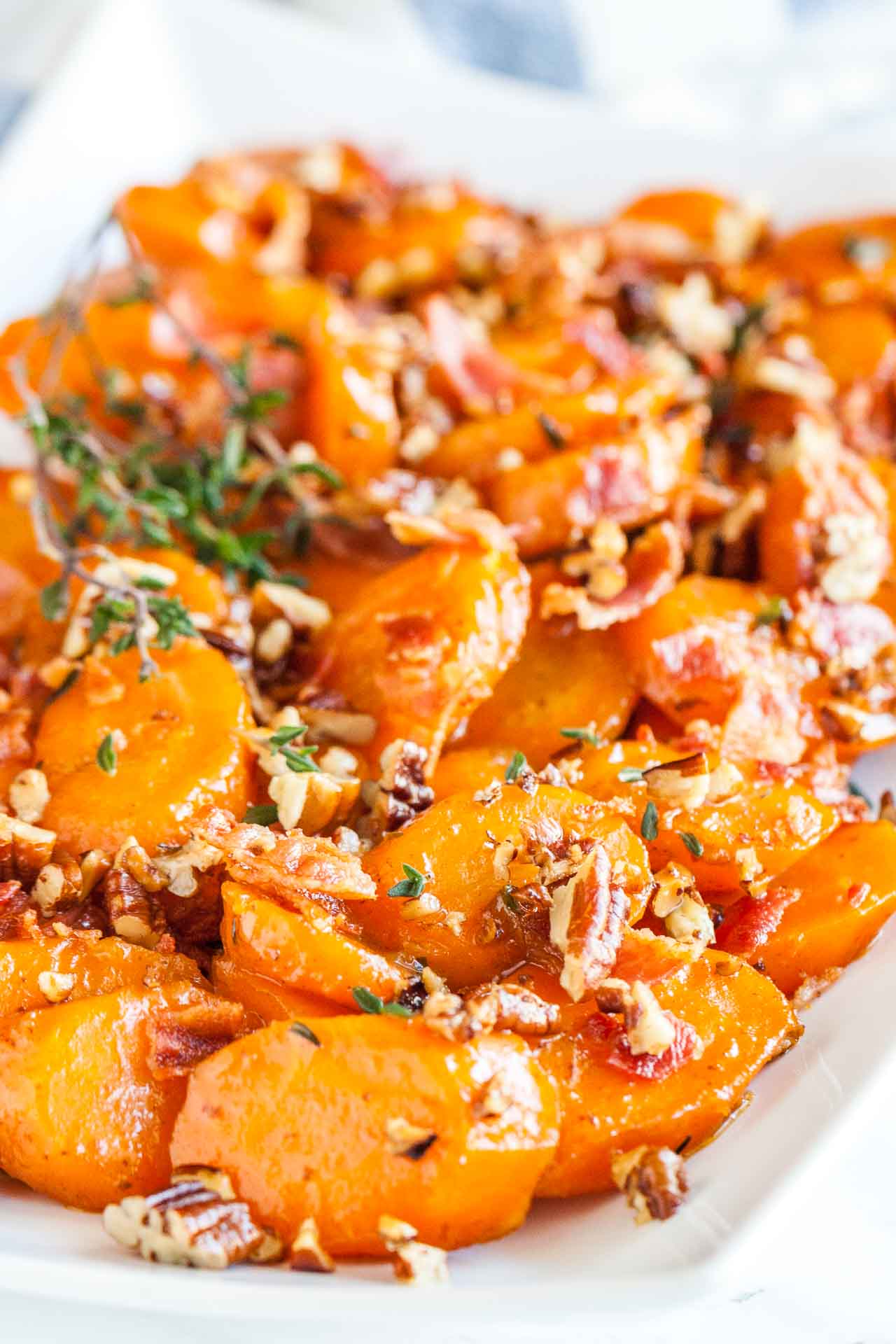 Close-up of a rectangular white plate of brown sugar-glazed carrots with bacon and pecans garnished with thyme.