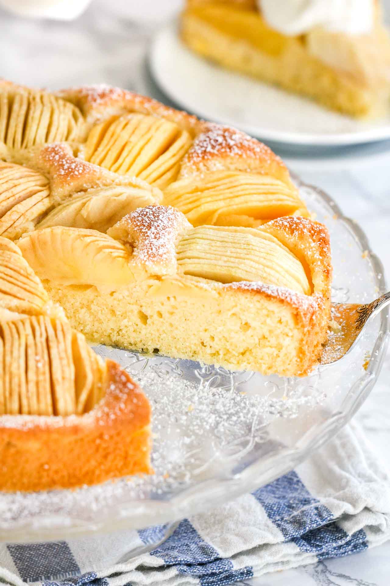 A cake with quartered apples sunken into the top on a glass serving platter.