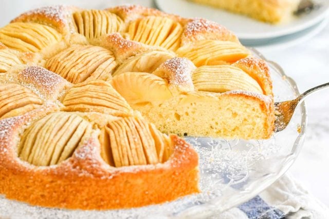 A cake with quartered apples sunken into the top on a glass serving platter.