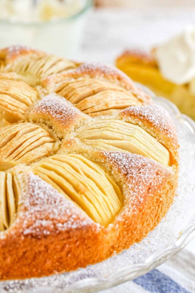 A whole cake with quartered apples sunken into the top on a glass serving platter.