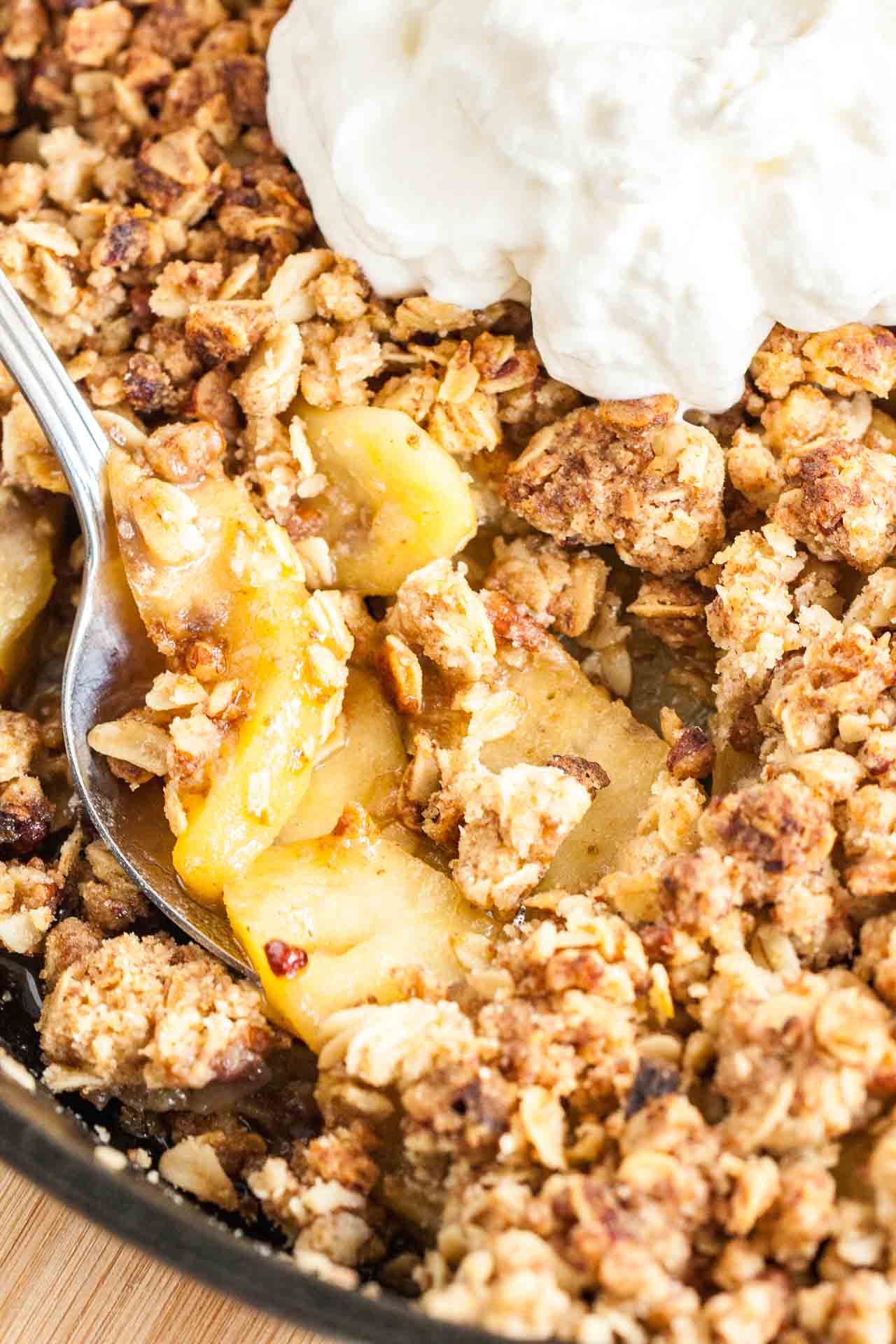 A baking pan with apple crisp topped with whipped cream and a spoon in it, lifting out a portion.