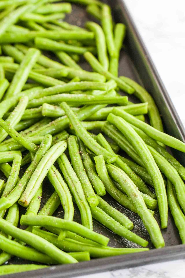 Uncooked green beans on a baking sheet with salt and pepper.