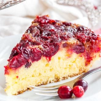 A slice of upside-down cranberry cake on a white plate with a fork, garnished with cranberries and Christmas stars in the background