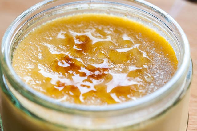 Close-up of a glass of creme brulee on a wooden cutting board with a lightly melted and browner sugar top.