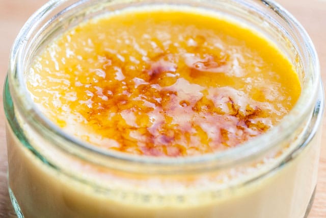 Close-up of a glass of creme brulee on a wooden cutting board with a melted and browner sugar top.