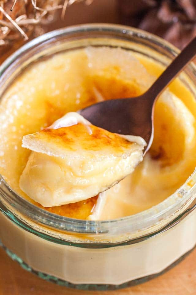 Close-up of a glass of creme brulee with a bronze spoon cracking its top.