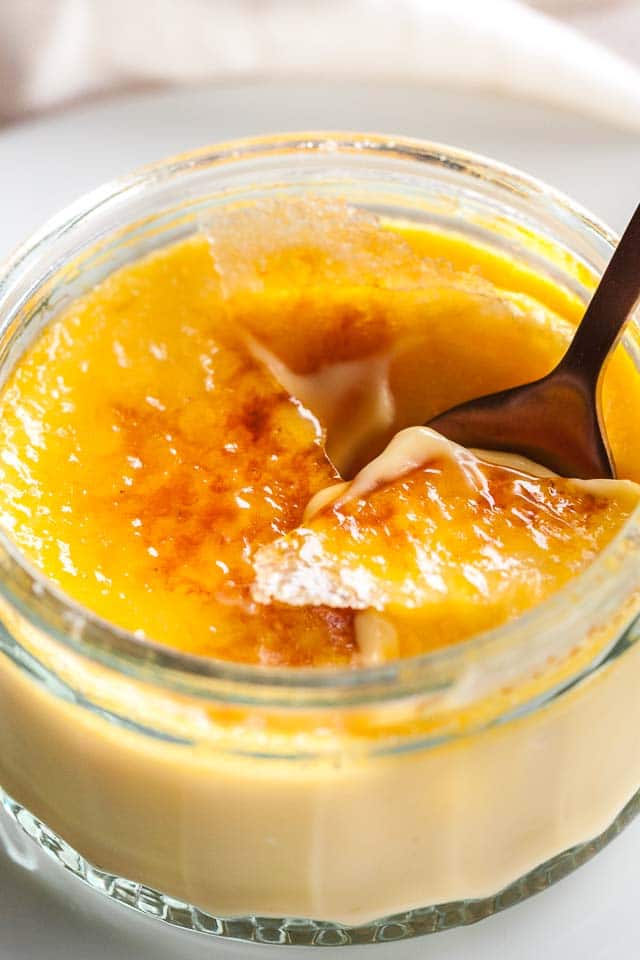 Close-up of a glass of creme brulee with a bronze spoon cracking its top.